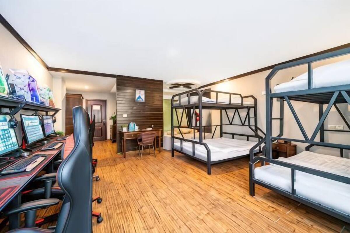 A dormitory room with bunk beds, a desk with a computer, and a chair.