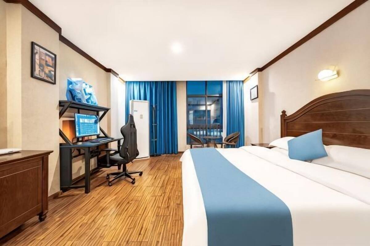 A hotel room with a bed, desk, chair, and a view of the outside.