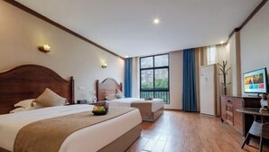Habitación de hotel con dos camas, televisión, escritorio y ventana con vistas a edificios.