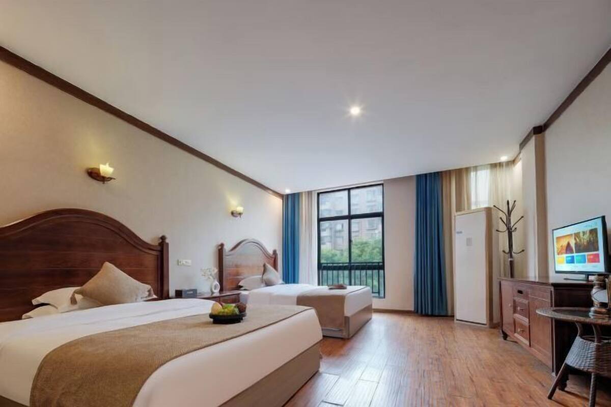A hotel room with two beds, a television, a desk, and a window with a view of buildings.