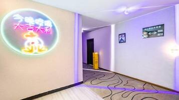 A hotel corridor with a neon sign, directional signs, and a patterned carpet.