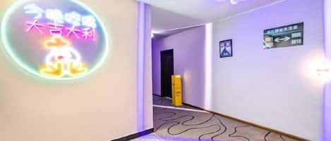 A hotel corridor with a neon sign, directional signs, and a patterned carpet.
