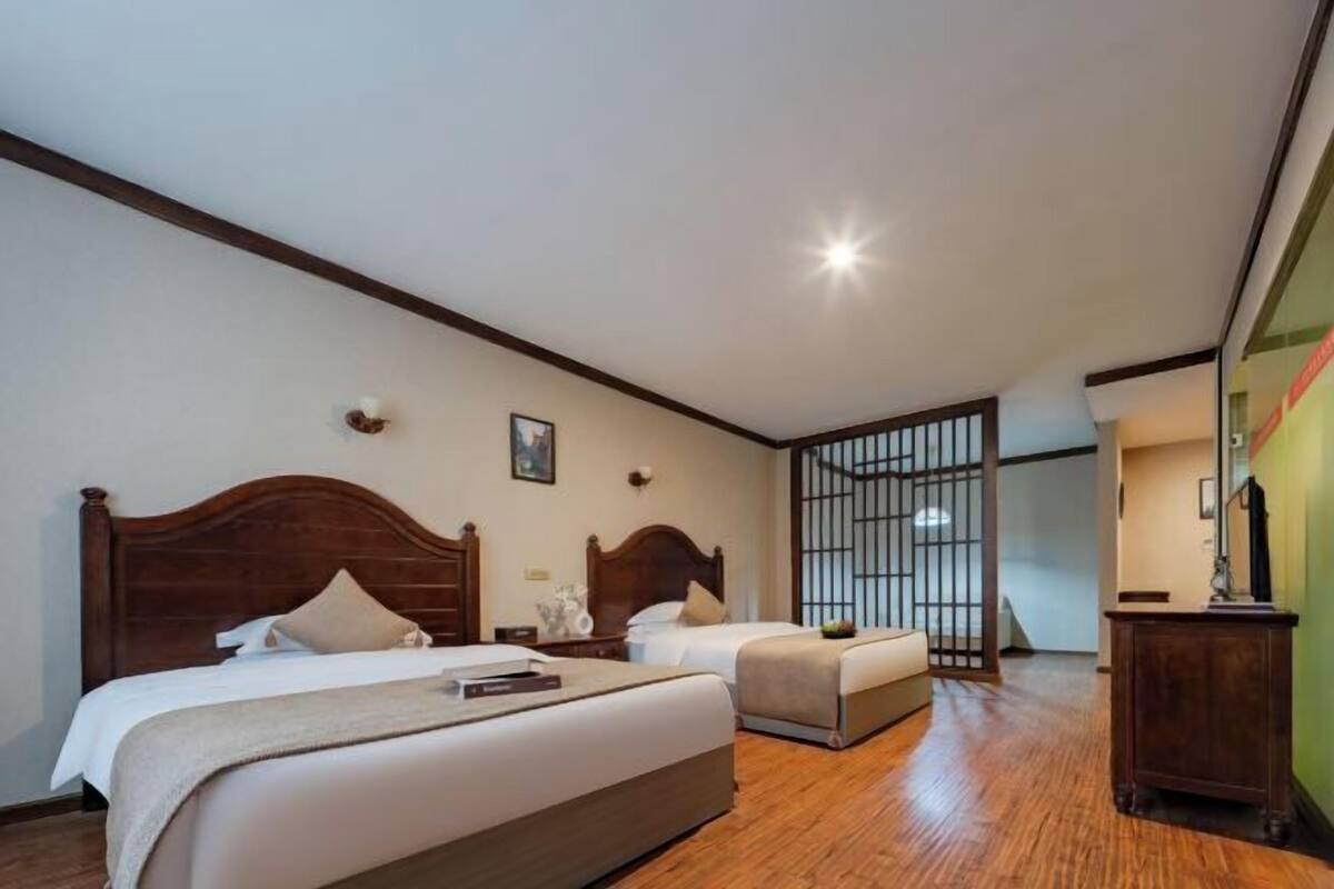 A hotel room with two beds, wooden headboards, a nightstand, a desk, and a partition with bars.