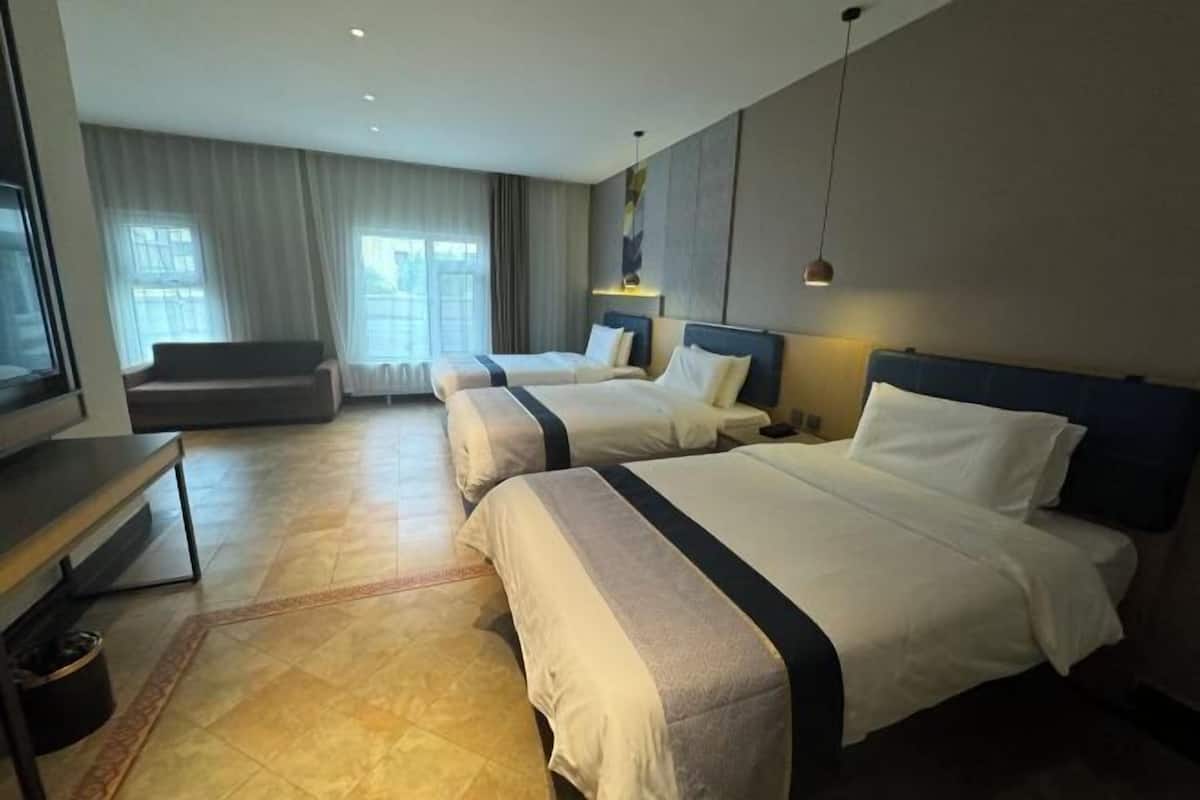 A hotel room with two beds, a sofa, a desk, and a large window with curtains.