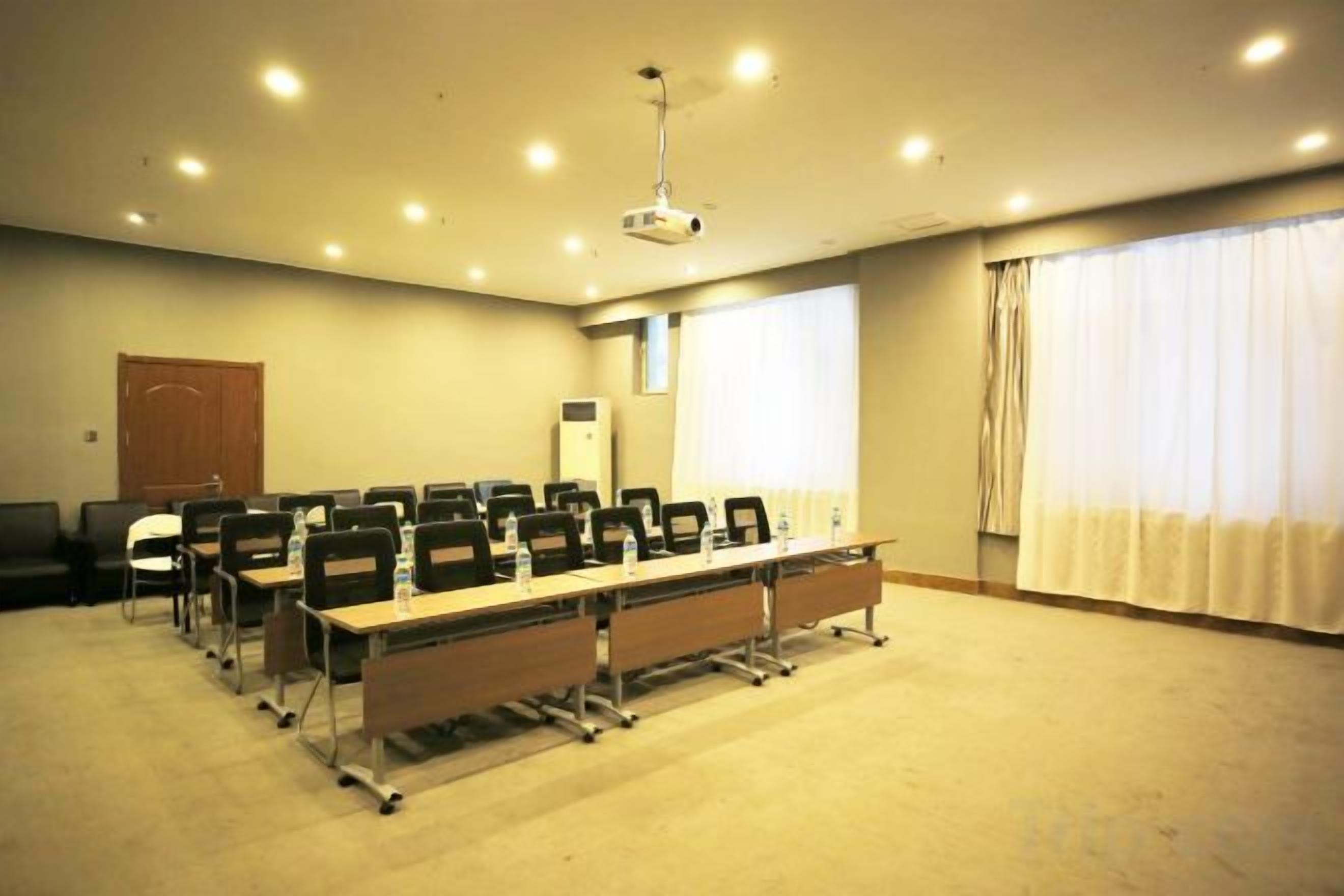 Uma sala de conferência com uma mesa comprida, cadeiras, um projetor e uma janela com cortinas.