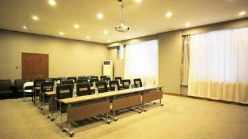 Uma sala de conferência com uma mesa comprida, cadeiras, um projetor e uma janela com cortinas.