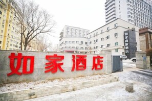 L’entrée d’un hôtel, reconnaissable à son grand panneau rouge, une allée bordée de portails et les bâtiments environnants.