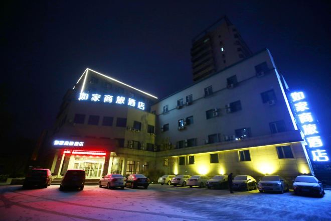 A hotel with multiple floors, a parking lot with several cars, and illuminated signage.