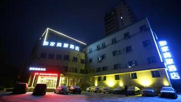 Un hotel de varios pisos, un estacionamiento con varios autos, y señalización iluminada.