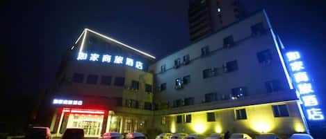 A hotel with multiple floors, a parking lot with several cars, and illuminated signage.