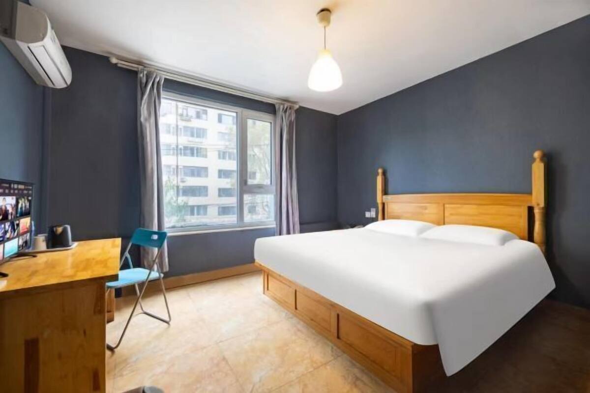 A hotel room with a bed, desk, chair, and window.