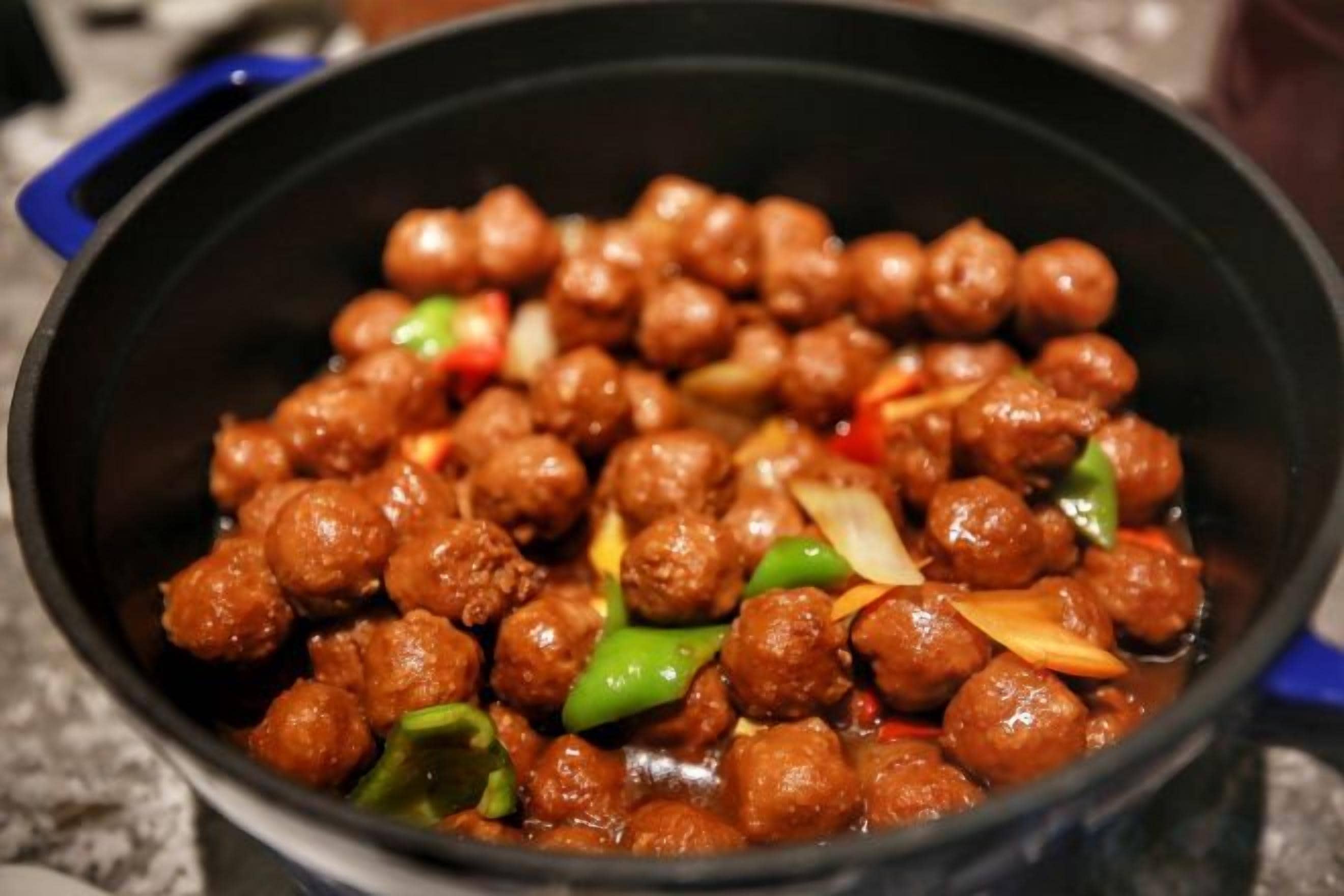Una olla negra con un guiso de albóndigas redondas y verduras en rodajas.