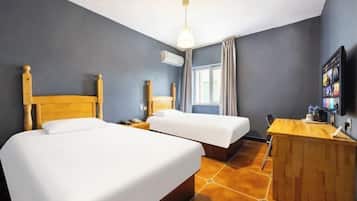 Habitación de hotel con dos camas, un escritorio, una silla, un equipo de aire acondicionado y un televisor.