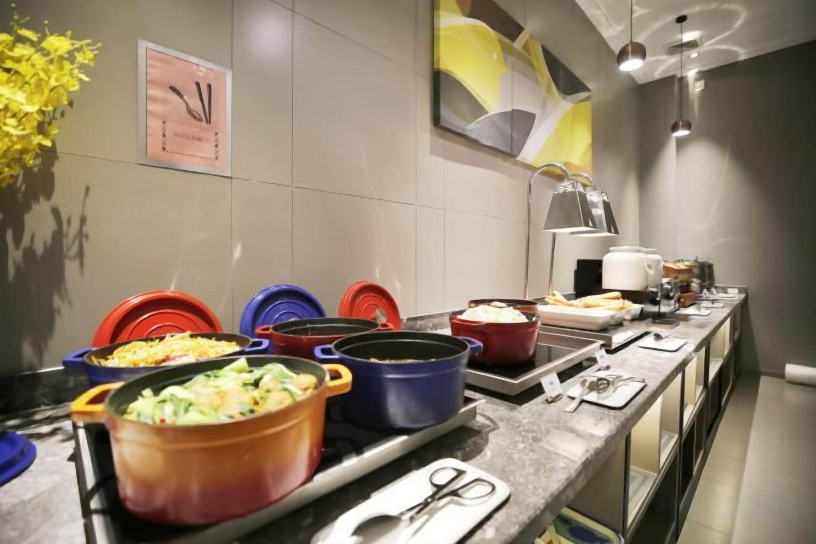 A buffet setup with various dishes in colorful pots, a clock, and a vase of yellow flowers on the wall.