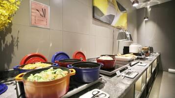 A buffet setup with various dishes in colorful pots, a clock, and a vase of yellow flowers on the wall.