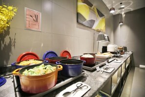 Un'attrezzatura per buffet con diversi piatti in contenitori colorati, una sveglia e un vaso di fiori gialli sulla parete.