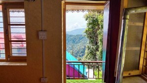 Une chambre avec un lit, une petite table et une fenêtre donnant sur un balcon d’où l’on peut admirer un paysage montagneux.