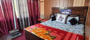 Une chambre à coucher avec une tête de lit en bois, une couvre-lit à motifs floraux, deux oreillers, une table de chevet et une chaise rouge.