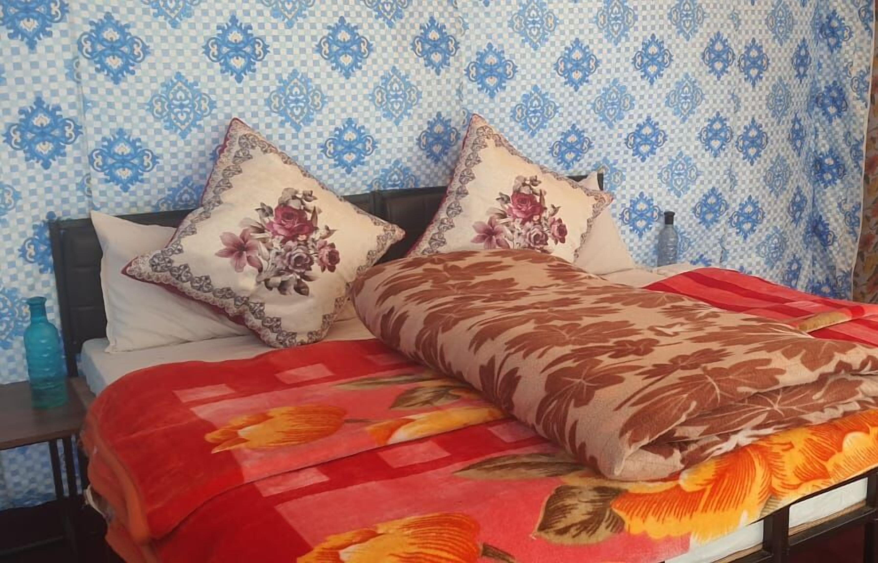 A bed with floral pillows and a red blanket with a leaf pattern.
