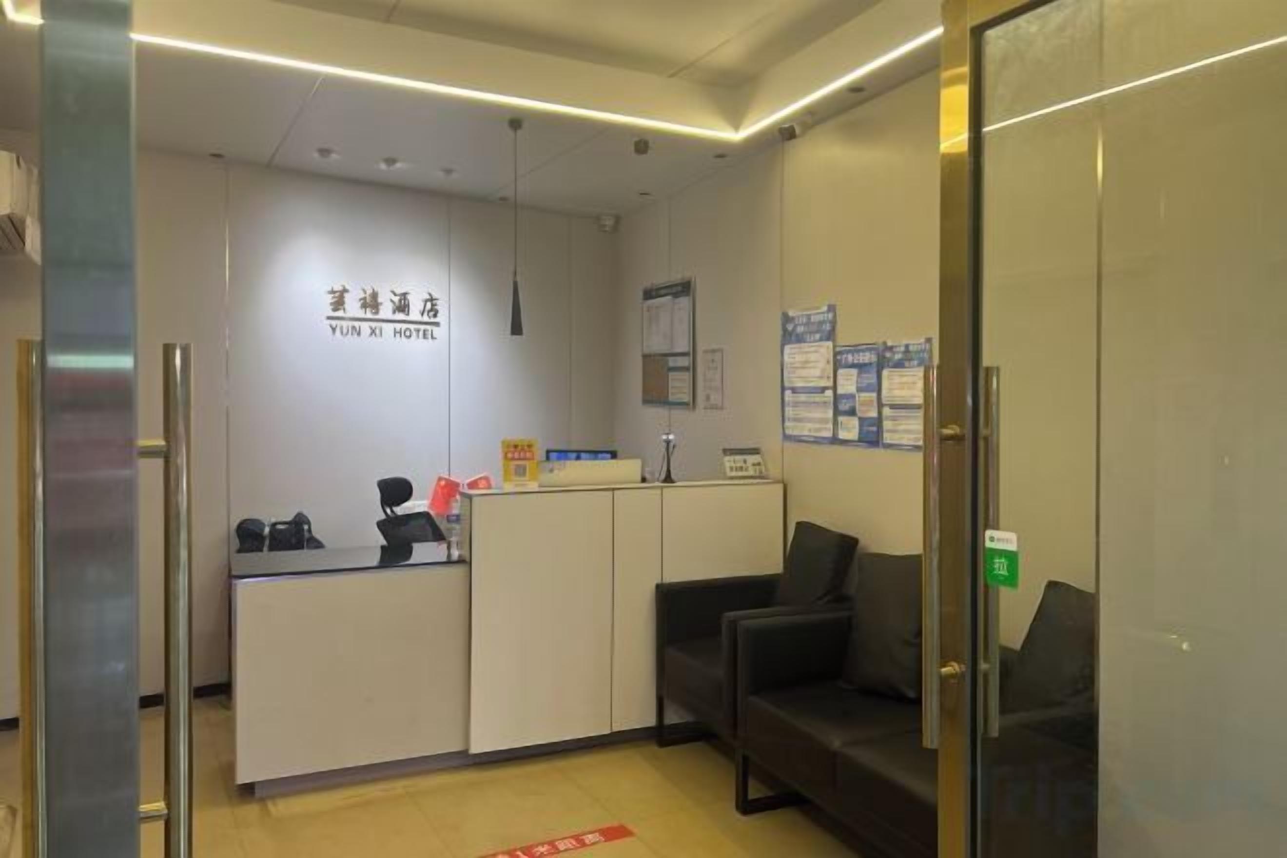 A reception desk with a sign reading 'YUN XI HOTEL' and a waiting area with a couch and a glass partition.