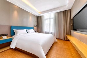A hotel room with a bed, a TV, a bedside table, and a window with curtains.
