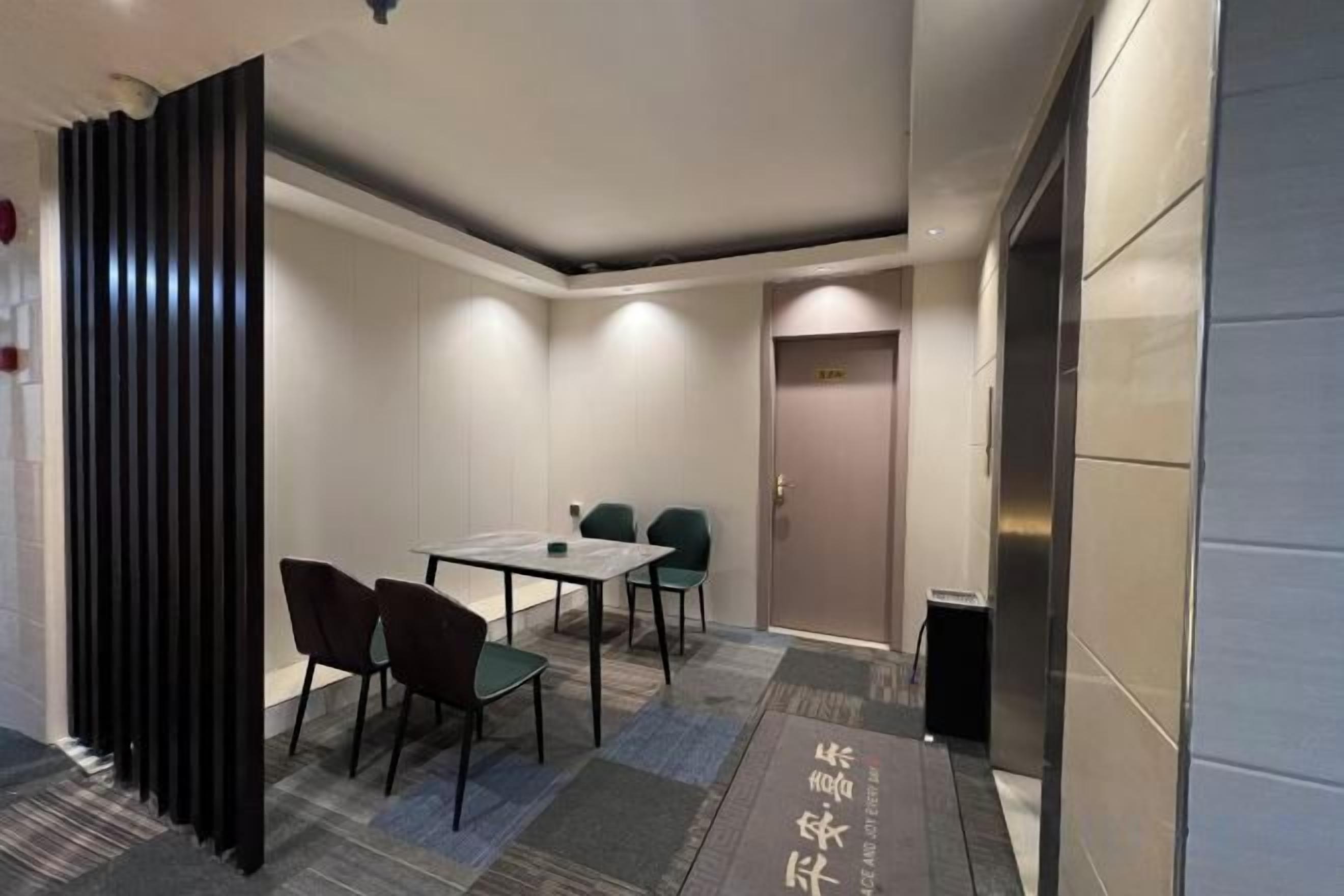 Habitación de hotel con una mesa de comedor, sillas, un panel negro y una puerta.