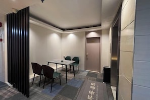 Een hotelkamer met een eettafel, stoelen, een zwarte scheidingswand en een deur.