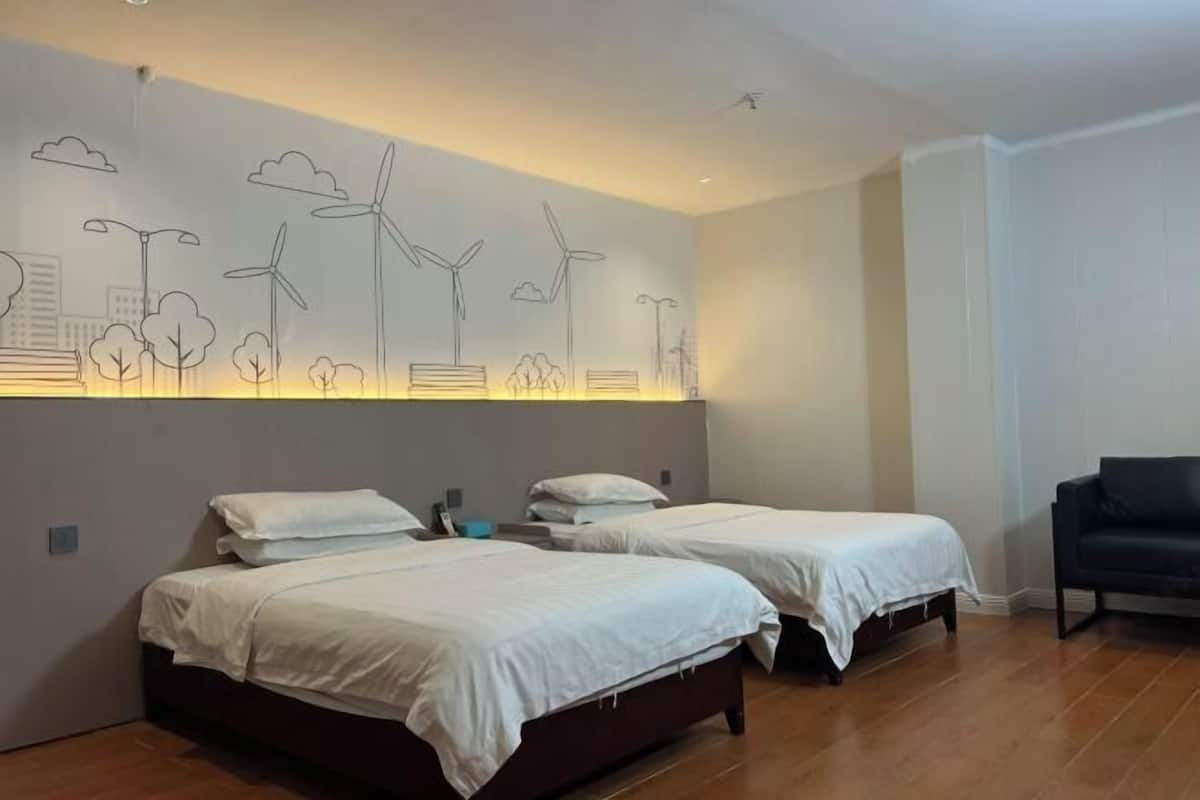 A hotel room with two beds, a wall mural of wind turbines and trees, and a dark-colored sofa.