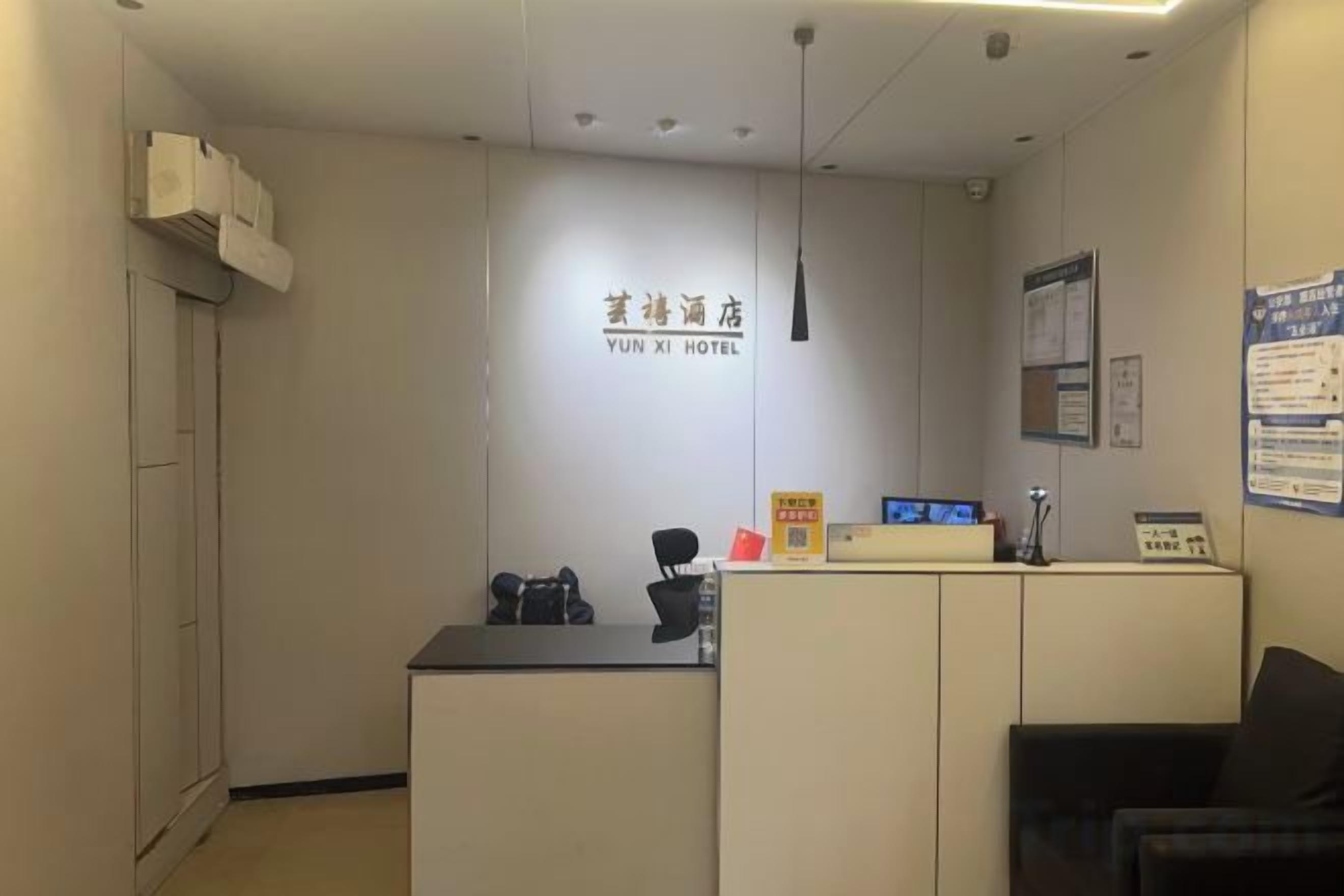 A reception desk with a sign for YUN XI HOTEL, a black chair, and a bulletin board on the wall.