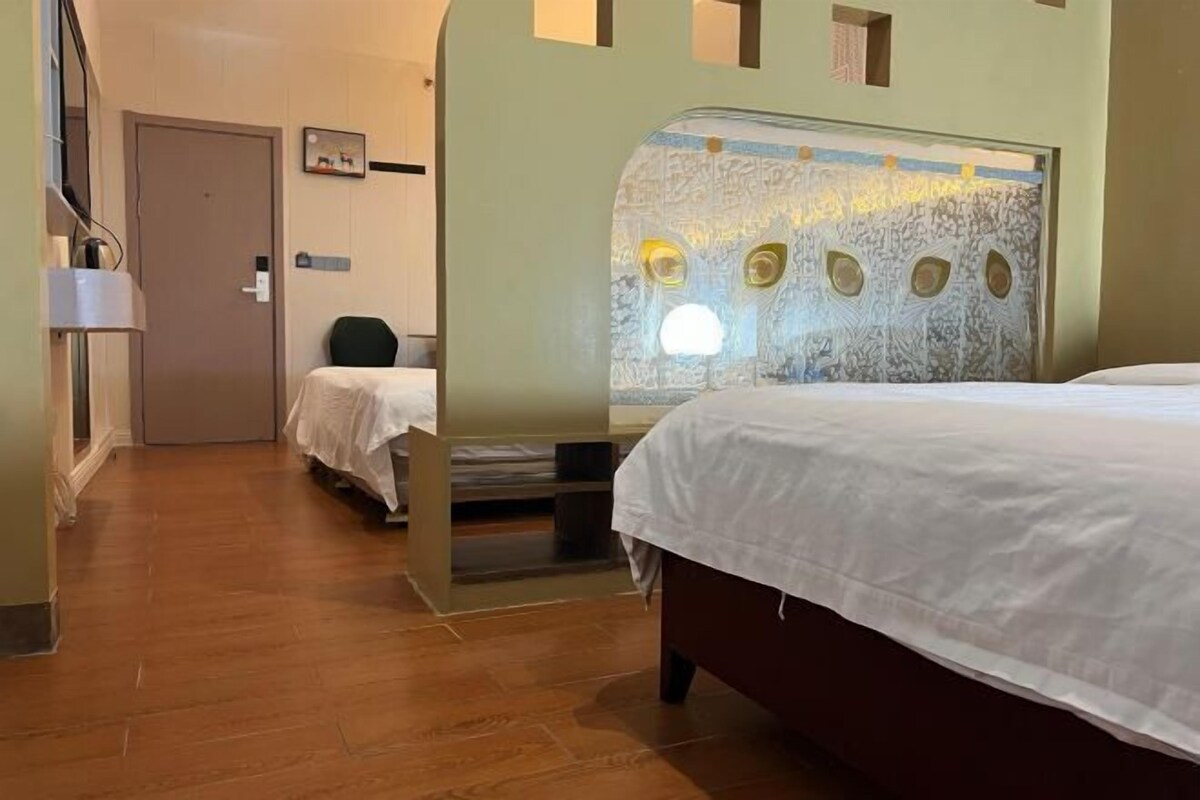 A hotel room with a large bed, a smaller bed, a desk, and a wall with a textured design.