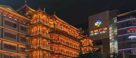 A traditional multi-story building with ornate architectural details, a modern building with a colorful logo, and a clear night sky.