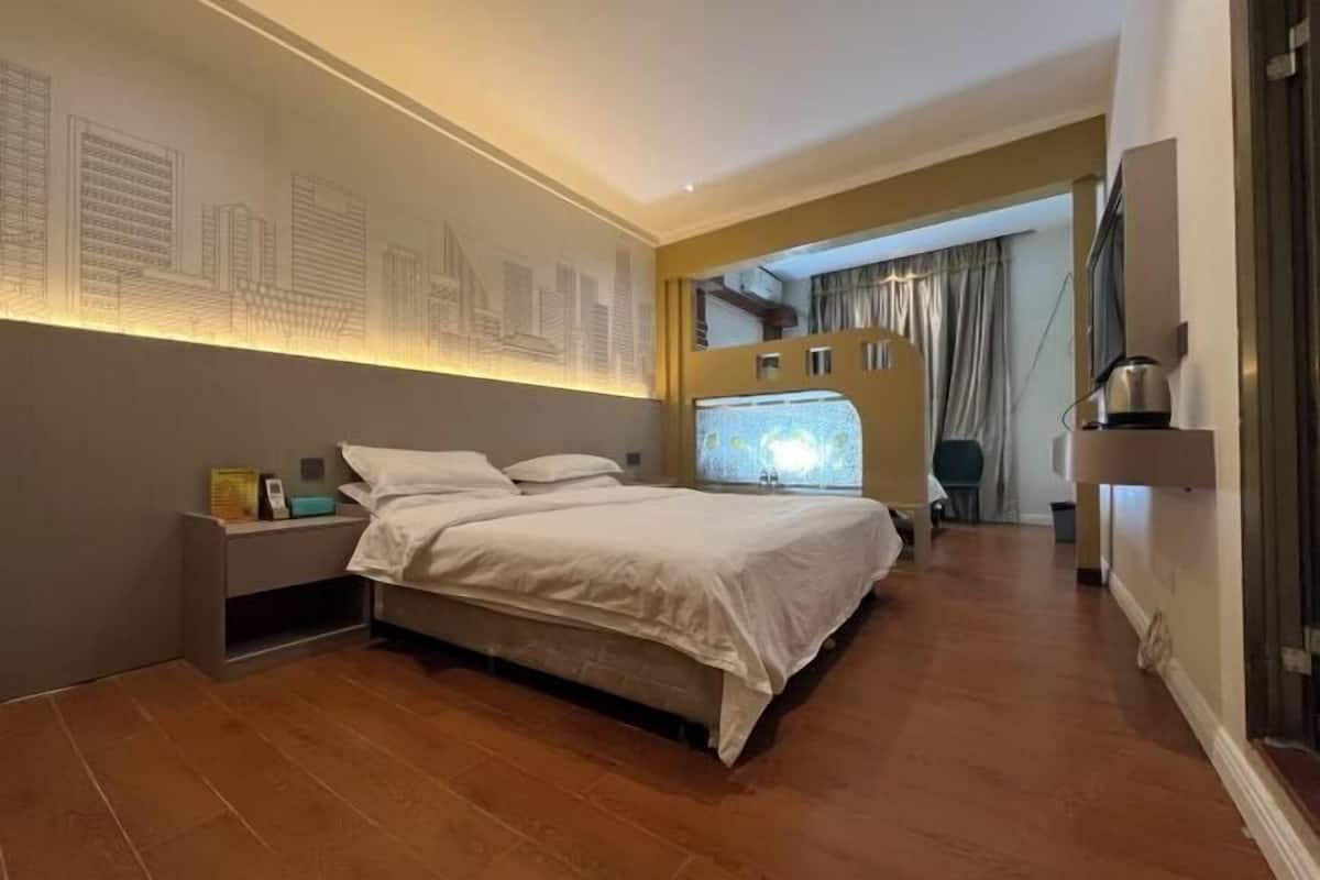 A modern bedroom with a large bed, a nightstand, a wall-mounted TV, and a cityscape mural.