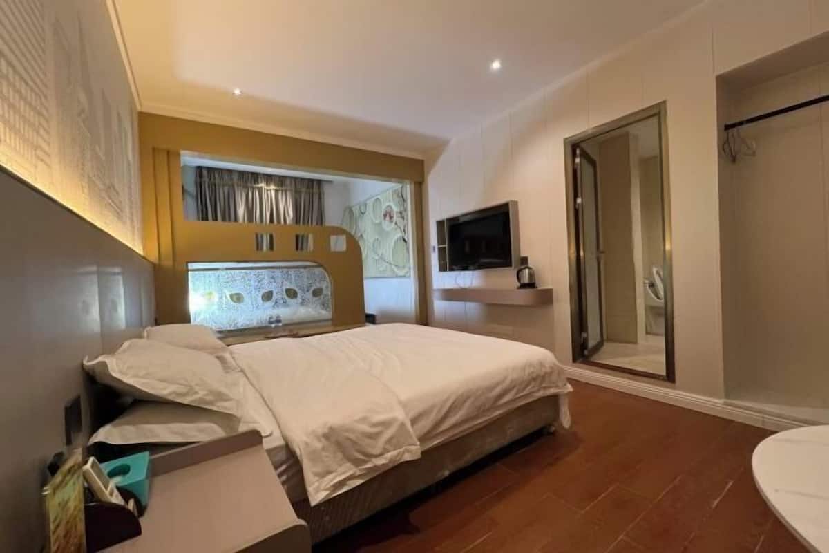 A bedroom with a bed, a TV, a shower, and a bathroom.