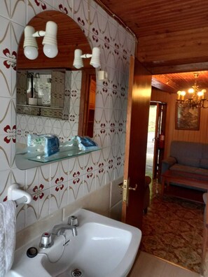 A bathroom with a white sink, a mirror, and a glass shelf with toiletries.