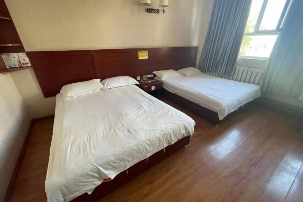 Quarto de hotel com duas camas, uma cabeceira de madeira, uma mesinha de cabeceira e uma janela com cortinas.