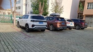 Una hilera de coches estacionados en un área pavimentada, con edificios al fondo.