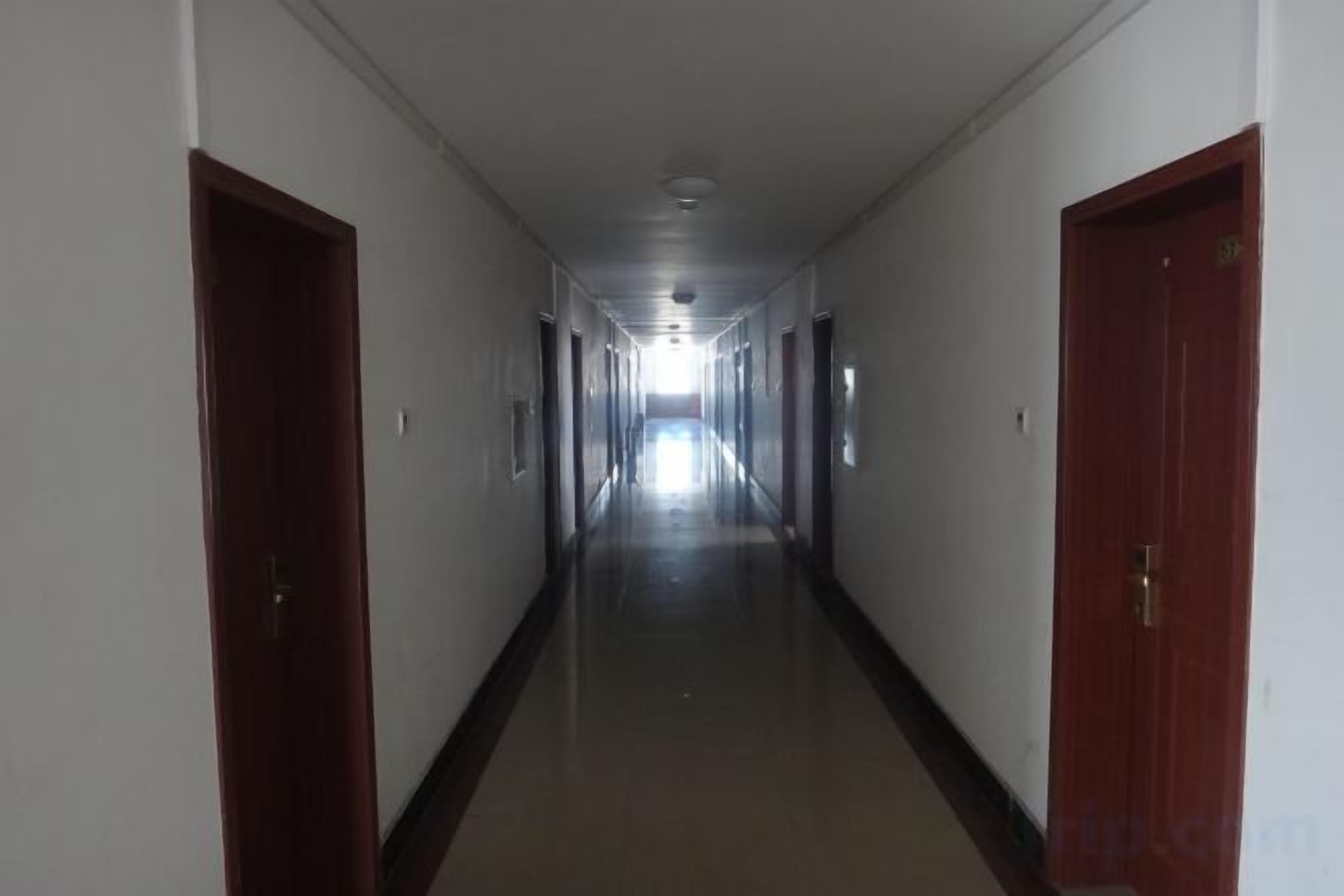 A long, narrow hallway with doors on both sides, leading to a bright end.