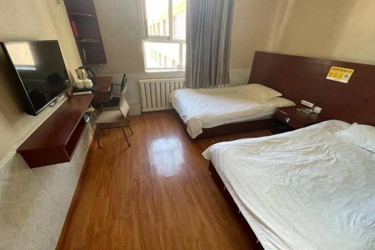 Quarto de hotel com duas camas, televisão, escrivaninha e janela com cortinas.