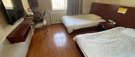 A hotel room with two beds, a TV, a desk, and a window with curtains.