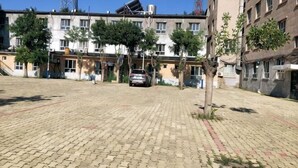 Un patio empedrado con un coche, árboles y edificios de varios pisos al fondo.