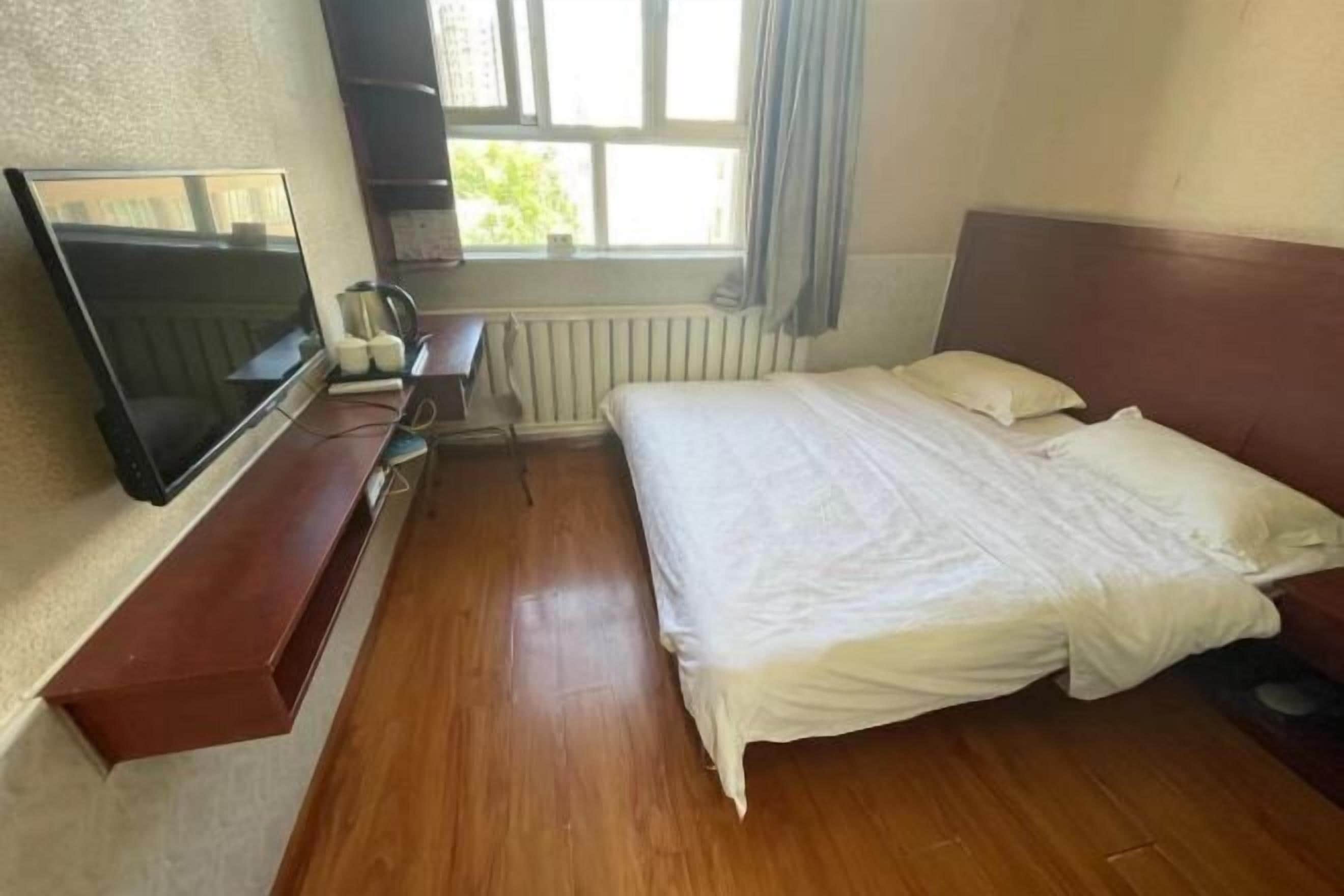 Una stanza con un letto, una TV su un mobile, un termosifone e una finestra con tende.