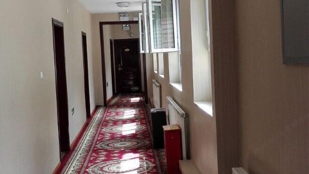 Un pasillo con alfombra estampada, un radiador y una ventana con persianas.