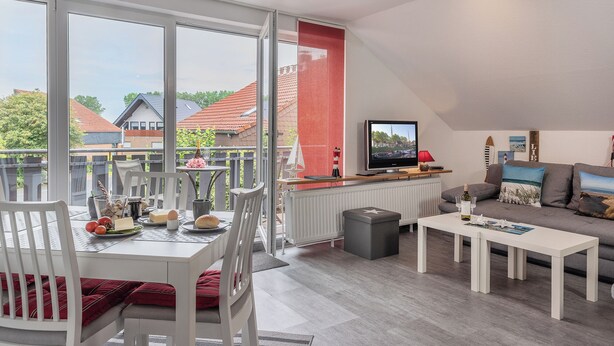 A modern living room with a dining area, a television, and a view of the neighborhood.