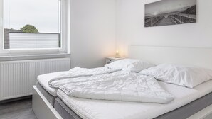 A bedroom with a bed, a window, a bedside table with a lamp, and a wall-mounted picture.