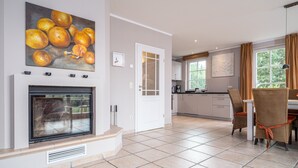 A spacious kitchen with a tiled floor, a dining area with chairs, a fireplace, and a painting of oranges on the wall. - Semi-detached house Villa an der Düne in the Baltic seaside resort of Dierhagen (Ostseebad Dierhagen)