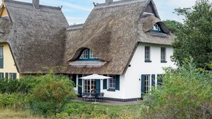 A house with a unique thatched roof design and a small patio area with outdoor furniture. - Semi-detached house Villa an der Düne in the Baltic seaside resort of Dierhagen (Ostseebad Dierhagen)