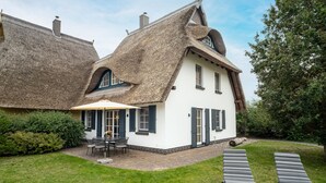 A traditional house with a thatched roof, a patio with outdoor furniture, and a well-maintained lawn. - Semi-detached house Villa an der Düne in the Baltic seaside resort of Dierhagen (Ostseebad Dierhagen)