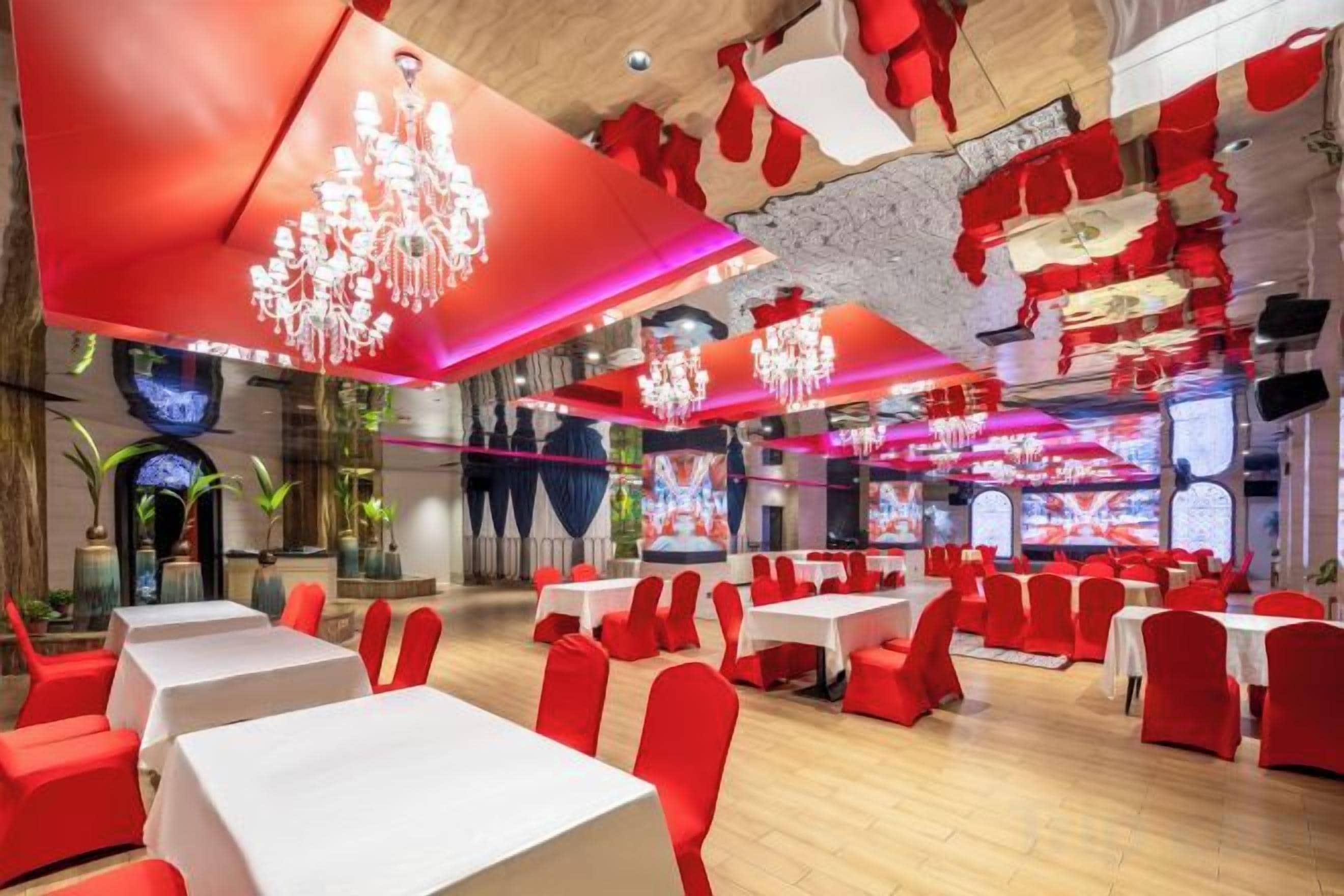 Un restaurante con varias mesas y sillas, una decoración en tonos rojo y blanco, y candelabros.