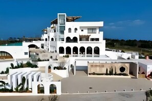 Un bâtiment blanc à plusieurs étages, doté de fenêtres en arc de cercle et d’une terrasse sur le toit.