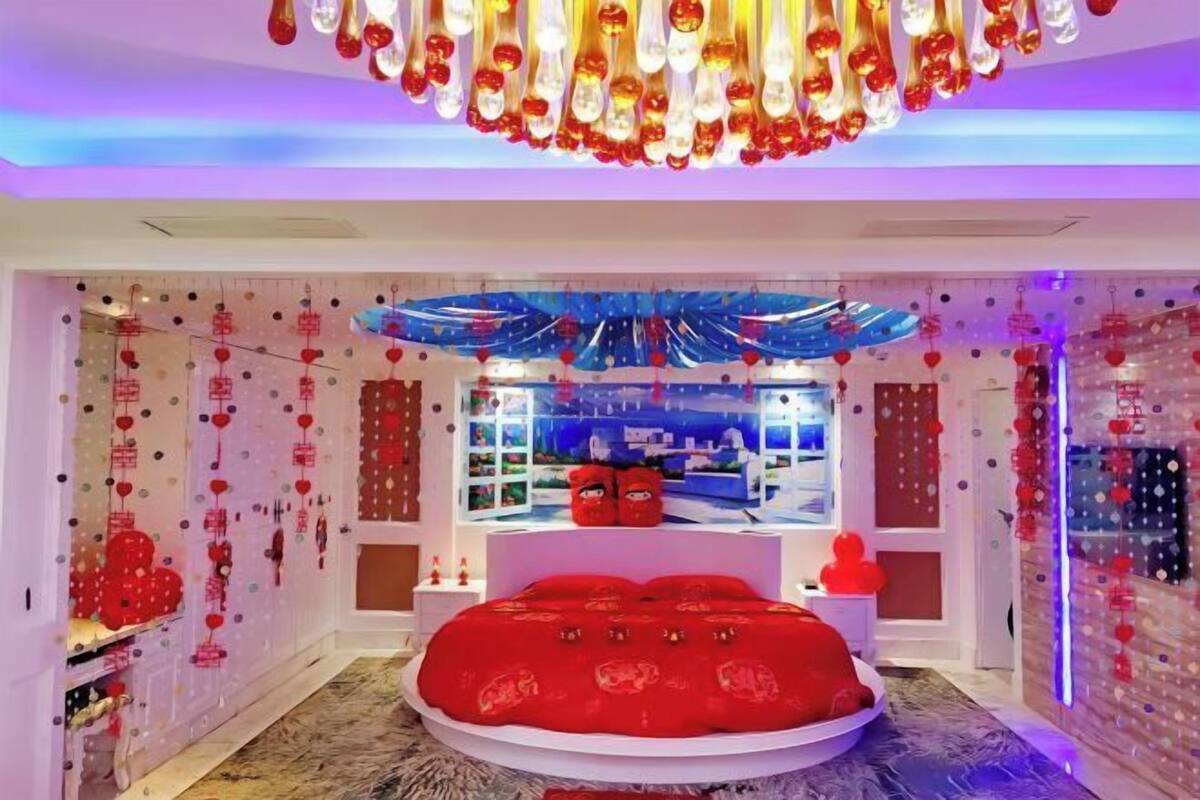 A modern bedroom with a circular bed, decorative wall hangings, and a unique ceiling light fixture.